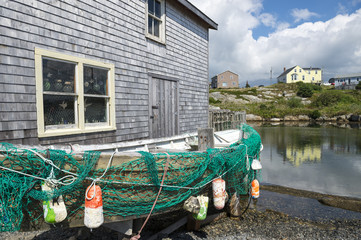 Fototapeta na wymiar Dilapidated old fishing boat rests next to a weathered shack on the rocky shore of a fishing village in Peggy's Cove, in Halifax, Nova Scotia, Canada