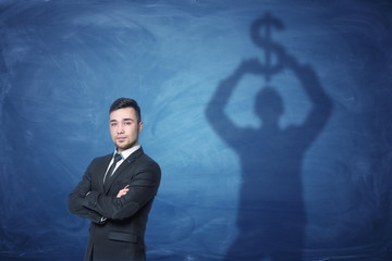 Businessman standing and shadow on the blackboard behind him holding dollar sign above his head