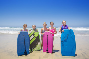 Cute group of kids standing by a boogie boards at the beach while playing in the ocean on vacation....