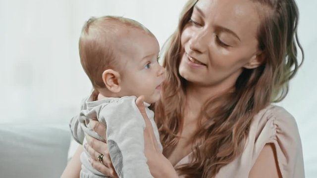 Medium shot of young mother holding fussy baby on her arms and kissing him