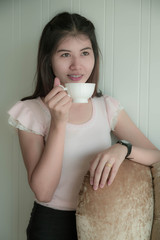 young cute and back hair Asia woman is drinking coffee standing on deluxe gold armchair.