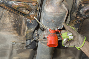 Man's hands in protective gloves repair a car in the service. Screw lubrication. Dirty job.