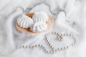 White airy zephyrs in the dish on the soft cloth with a decorative, small balls chain in heart form. Very beautiful surprise for someone in special moment.. Romance. Focus on the zephyrs.