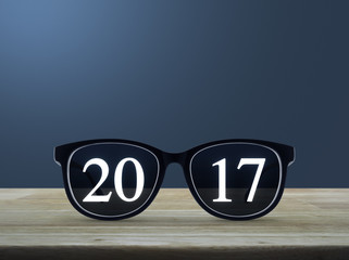 2017 text with eye glasses on wooden table over light blue gradient background, New year business concept