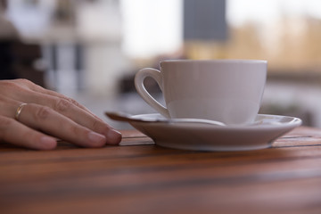  Hand of a young man on a wooden table in the cafe with cup of coffee in calm relaxing hand's posture,outdoor blur background