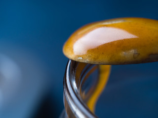 Macro closeup of spoon with salted caramel on glass jar over dark blue background