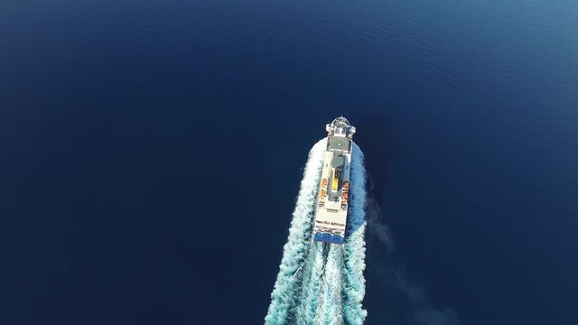 Flying over big vessel in the sea. Camera at high altitude follows a big ship. Foamy track behind the stern. Aerial view.