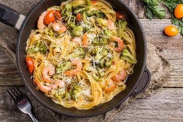 Pasta linguine with shrimps and broccoli in dripping pan on wooden background.