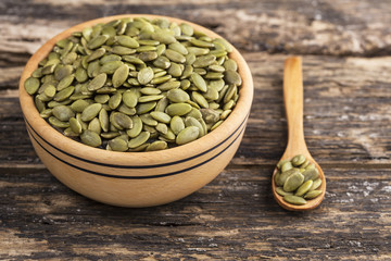 Wooden bowl and pumpkin seeds on wooden background