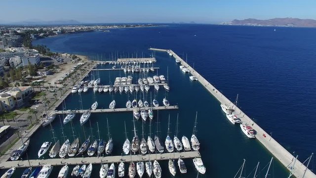 Flying over yacht marina in Kos island. Several boats are moored to the berths in the marina. Aerial view.
