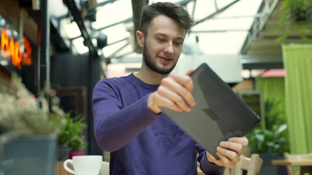 Happy boy sitting in the cafe and playing a game on tablet, steadycam shot
