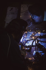 Craftsman welding pipe on a metal table in a workshop, hot sparks flying and reflections - obrazy, fototapety, plakaty