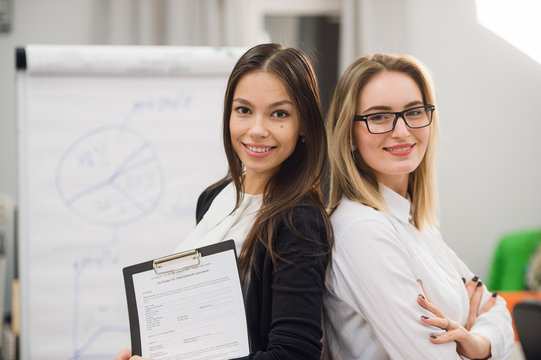 Two Business Women Standing At Office In Front Of Flip Chart