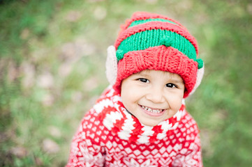 Half-length portrait of a little boy in elf hat and red sweater looking up and smiling. Child...