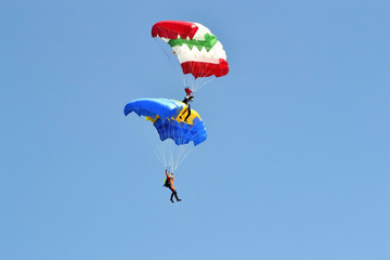 Two parachutists with multi-colored parachutes fly in the sky.