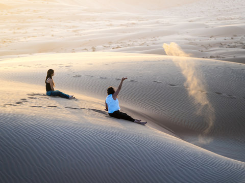 Two women sitting on dune in Rimal Al Wahiba desert, Al Raka, Oman