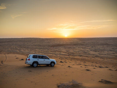 Oman, Al Raka, off-road vehicle parking on dune in Rimal Al Wahiba desert at sunset