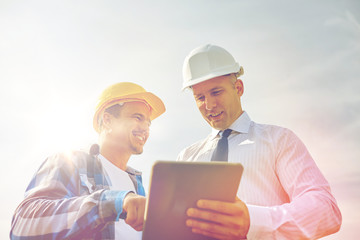 happy builders in hardhats with tablet pc outdoors