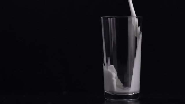 Pouring milk into glass on black background
