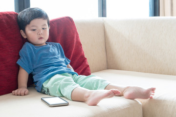 Boy is lying on the sofa and play with his smartphone