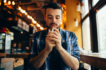 Young man is sitting in the restaurant and tasting a warm drink.
