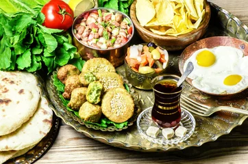 Photo sur Plexiglas Plats de repas Arabic cuisine,Egyptian breakfast of fried egg, plate of flafel,beans,pickles,chips, fresh organic vegetables,traditional backing bread and cup of tea in copper tray..
