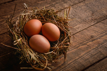 Chicken eggs in a wicker straw nest on wooden background