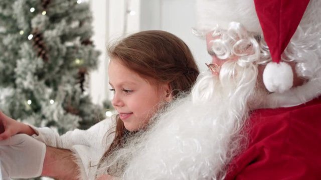 Santa Claus and cute little girl taking Christmas selfies on tablet