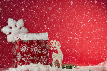 Reindeer and gift boxes on snow with snowfall on red background. Holidays decoration background