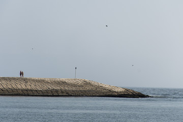 couple walking breakwater built concrete blocks pier ocean salalah oman