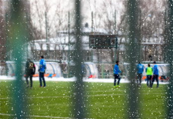 Snowy soccer field in December, frost and cold weather. Young people play football. Selective focus © svetlanais