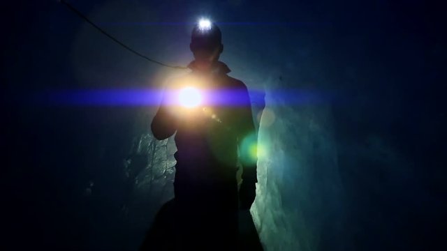 walking scientist holding flashlight exploring dark ice cave. blue light beaming  background.