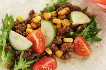 preparing homemade open tortilla with beef, frisee and corn