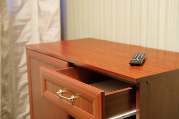 commode with an open drawer and a clicker on it in a hotel room