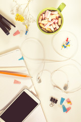 Office desk with cup of hot chocolate, phone, notebook, green plant and supplies. Flat lay white background. Coloring and processing photo.