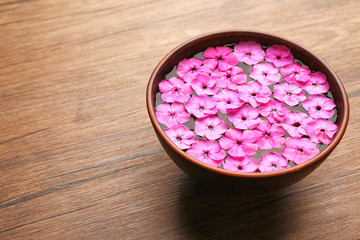 Bowl with water and pink flowers on wooden background