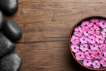 Spa stones and bowl with water and pink flowers on wooden background, top view