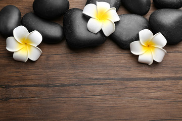 Spa stones and plumeria flowers on wooden background, top view