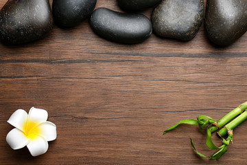 Fototapeta na wymiar Spa stones, plumeria flower and bamboo on wooden background, top view