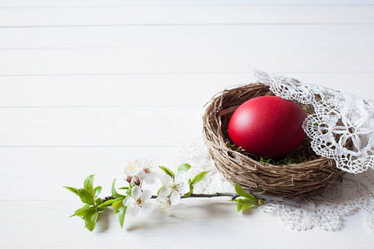 Easter white wooden background with a nest, red egg and branch with flowers, space for text