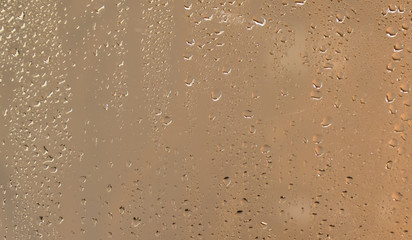 Water drops on a wet window with a gold colored defocused background abstract.