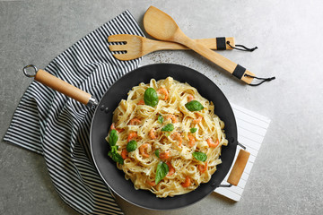 Pan with tasty alfredo pasta, kitchen board, napkin, spoon and fork on grey table