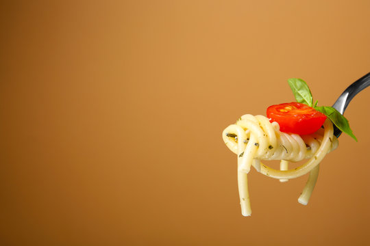 Fork with tasty pasta, tomato and basil on color background, close up view