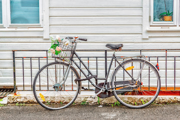 Fototapeta na wymiar Parked vintage bicycle with basket with flat forward tire at white wooden house background. Norway, Bergen.