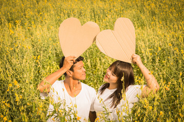 asian couple holding heart symbol in yellow field at summer time