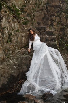 Young woman with blue eyes dressed bride sitting on a stone stairs in the countryside near a river just before marriage. 
