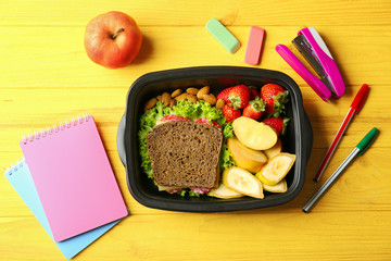 Lunch box with food and stationery on wooden background, top view © Africa Studio