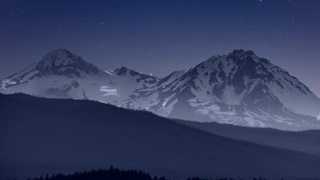 Starry sky and clouds slip past majestic mountains, time lapse.
