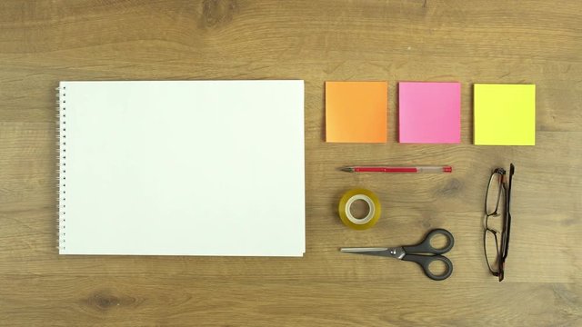 Sped up hand making drawing and sketching movements over a blank white notepad, next to sticky notes and office material. Easy to add your own line art, sketch or text on paper.