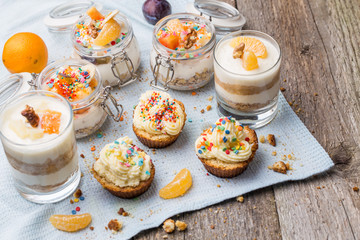 Homemade desserts - biscuits with yogurt, tangerines and walnuts in glass, oats with fresh fruit in glass jar and cupcakes with white frosting and sprinkles.
